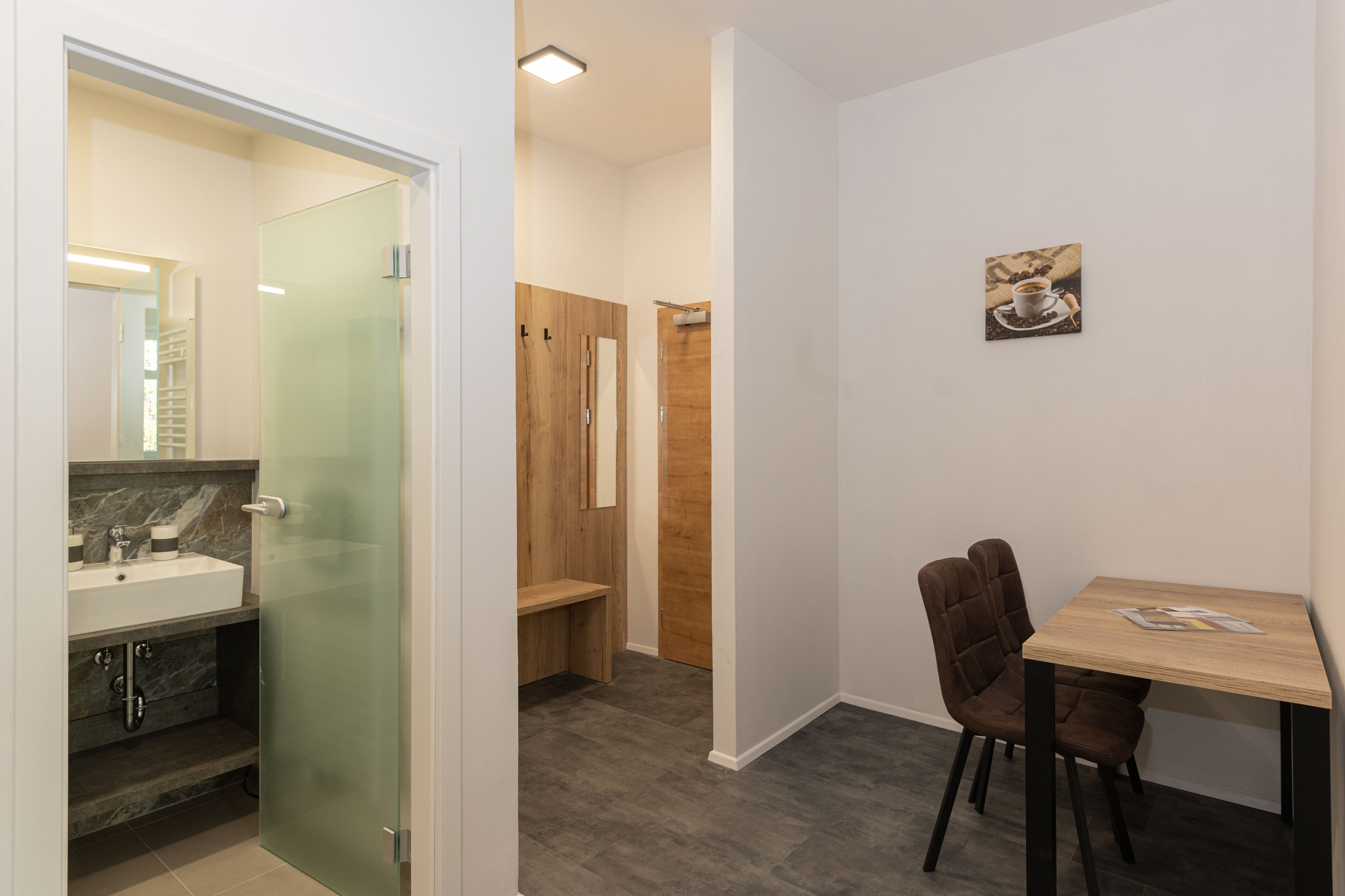 A modern bathroom with a glass shower enclosure, a wooden vanity, and a small table with a chair.