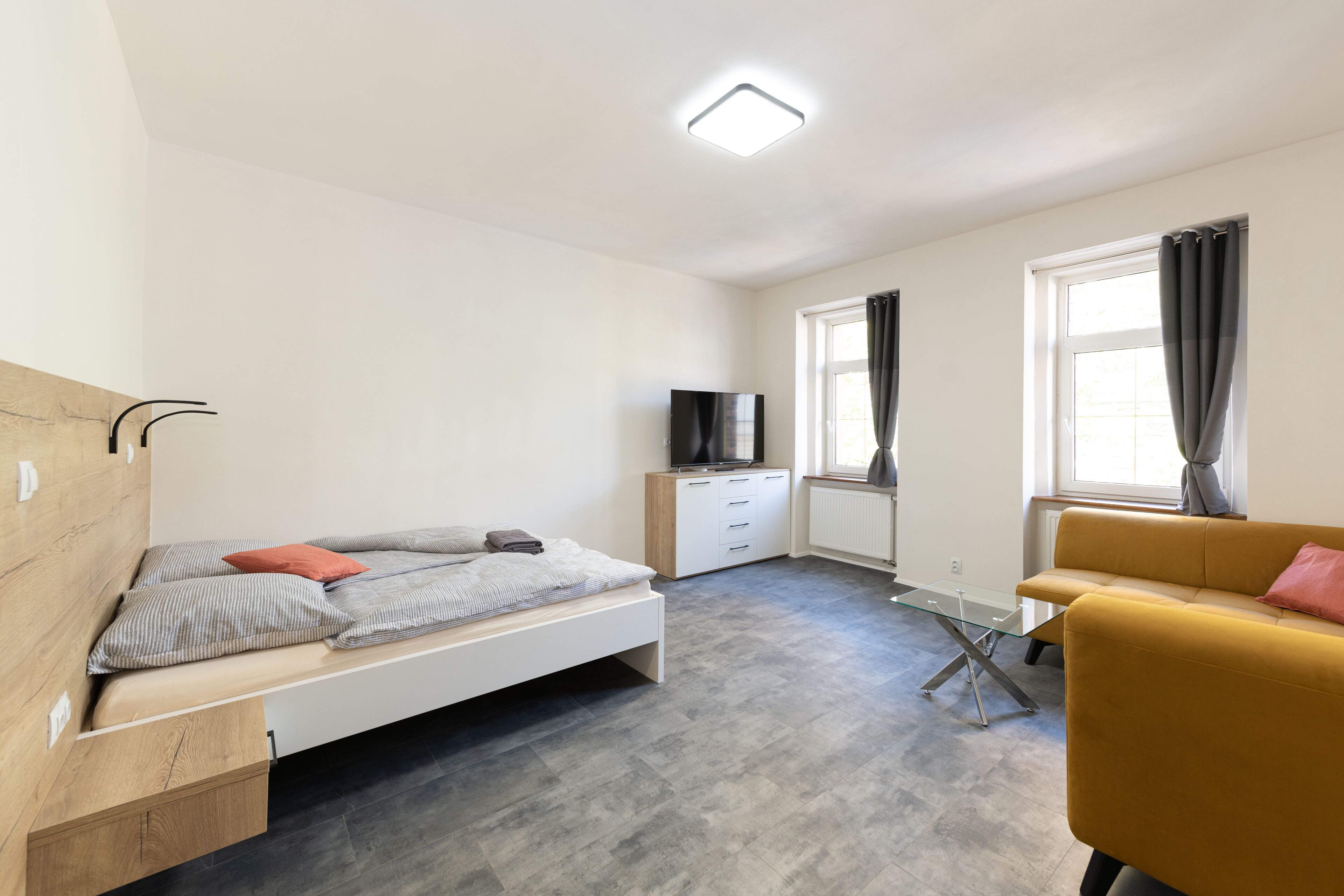 A modern bedroom with a bed, a sofa, a TV, and a window with curtains.