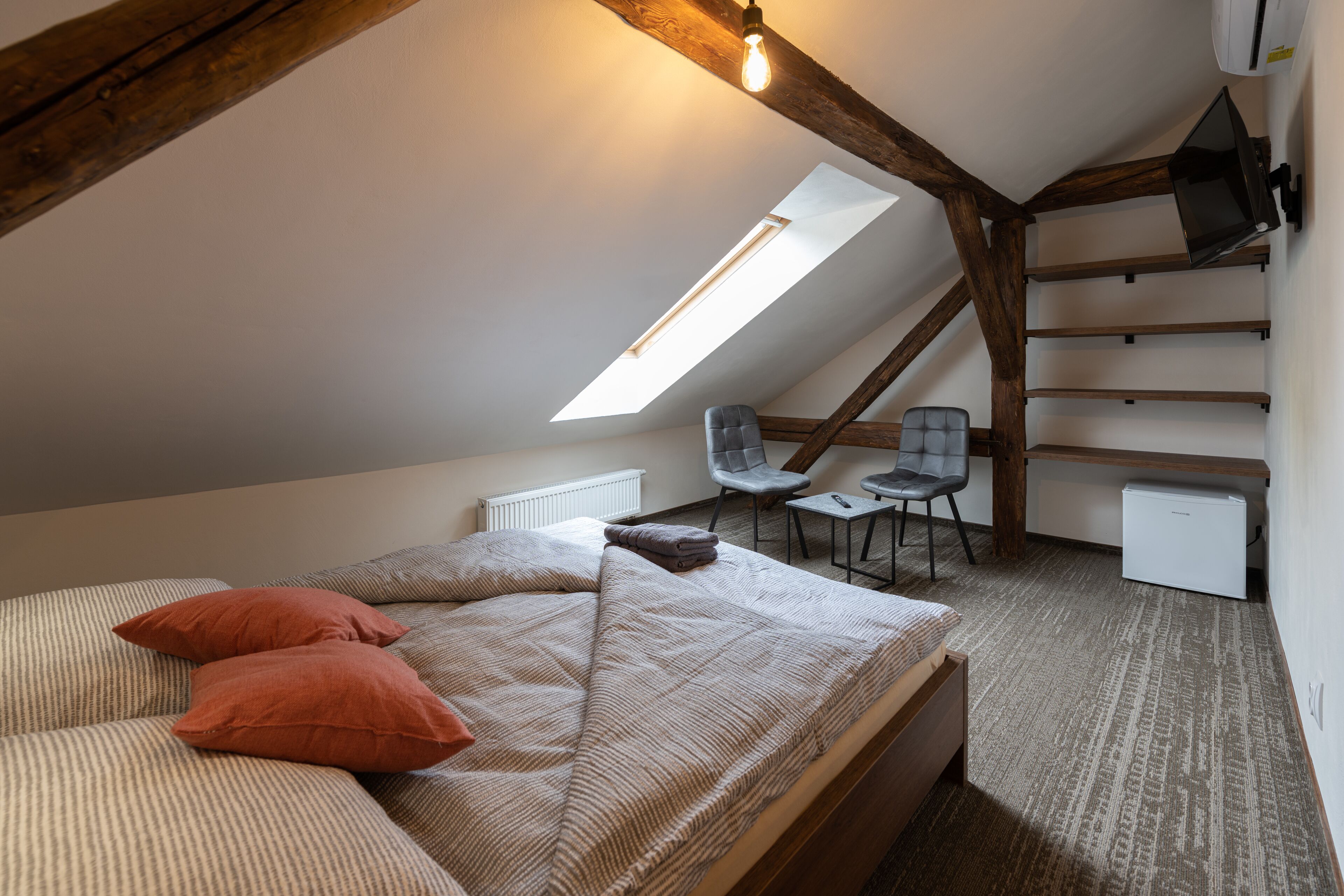 Een slaapkamer met een schuine kap, een bed, een bureau en een stoel.