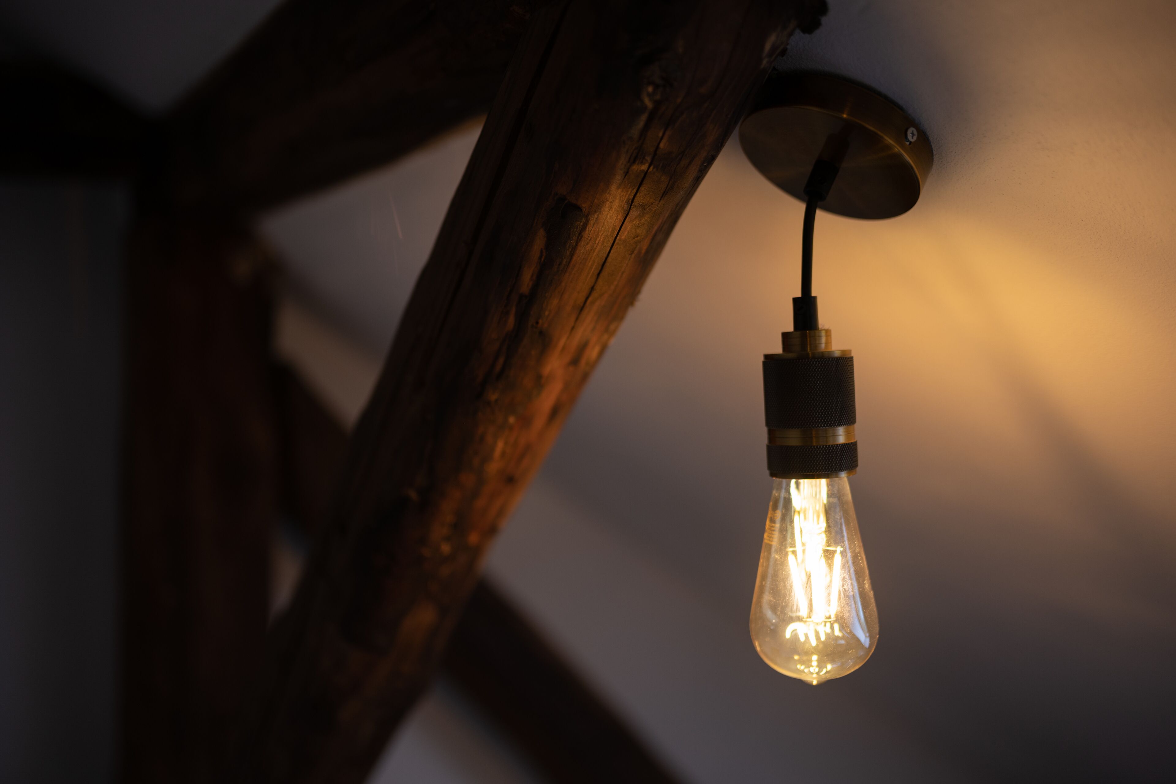 A single light bulb hanging from a wooden beam.