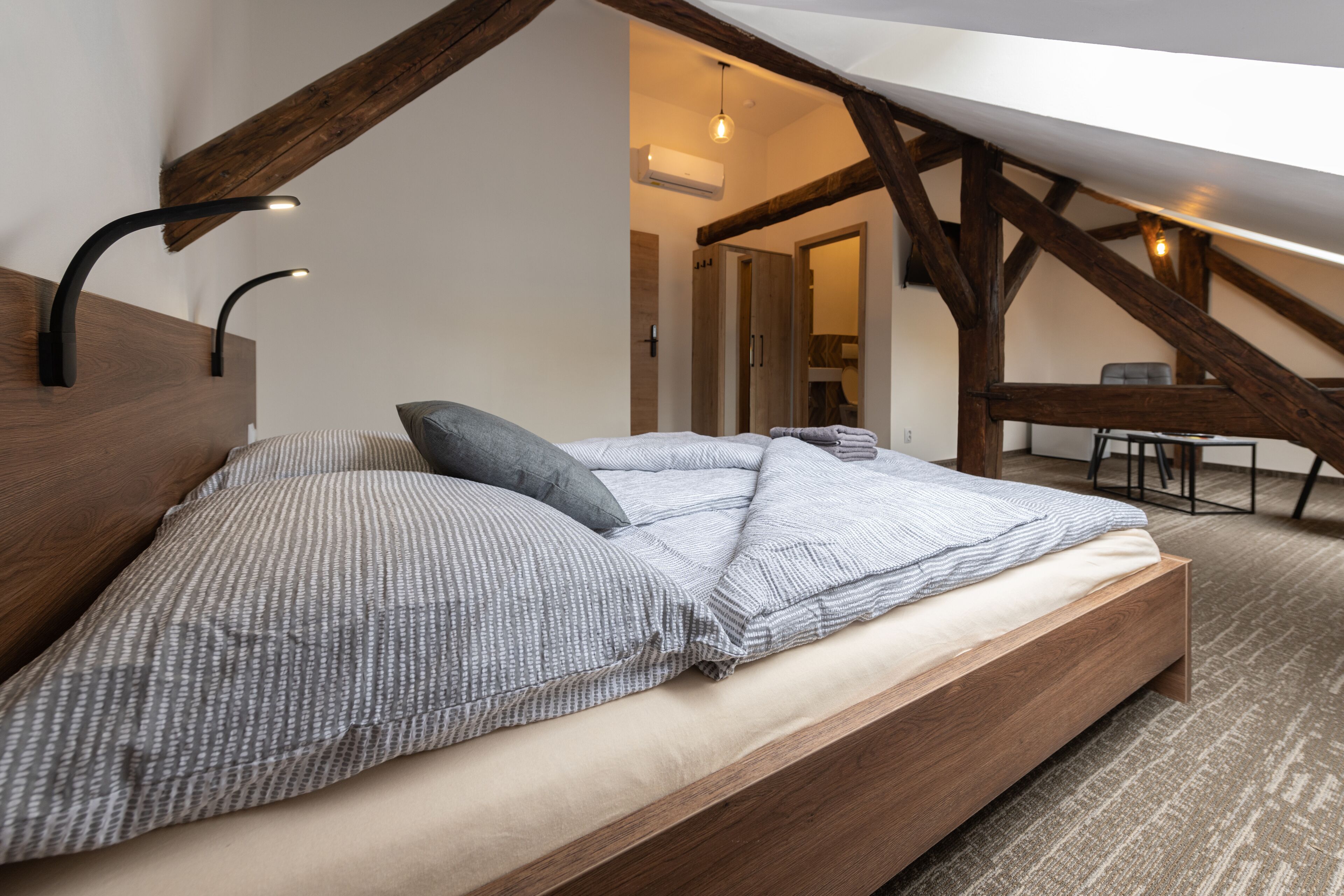 Un dormitorio con cama de madera, un escritorio y una silla en una habitación estilo loft con vigas a la vista.