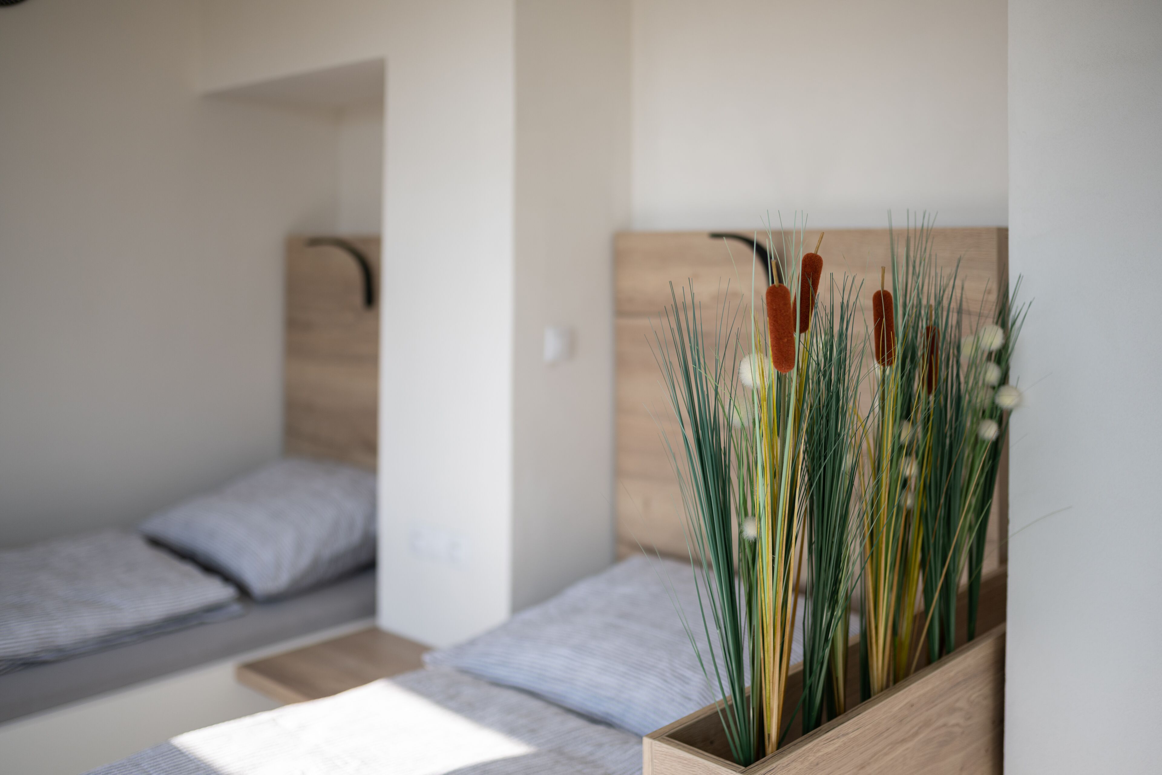 Un dormitorio con dos camas individuales, cabecera de madera y una pequeña mesita de madera con una planta.
