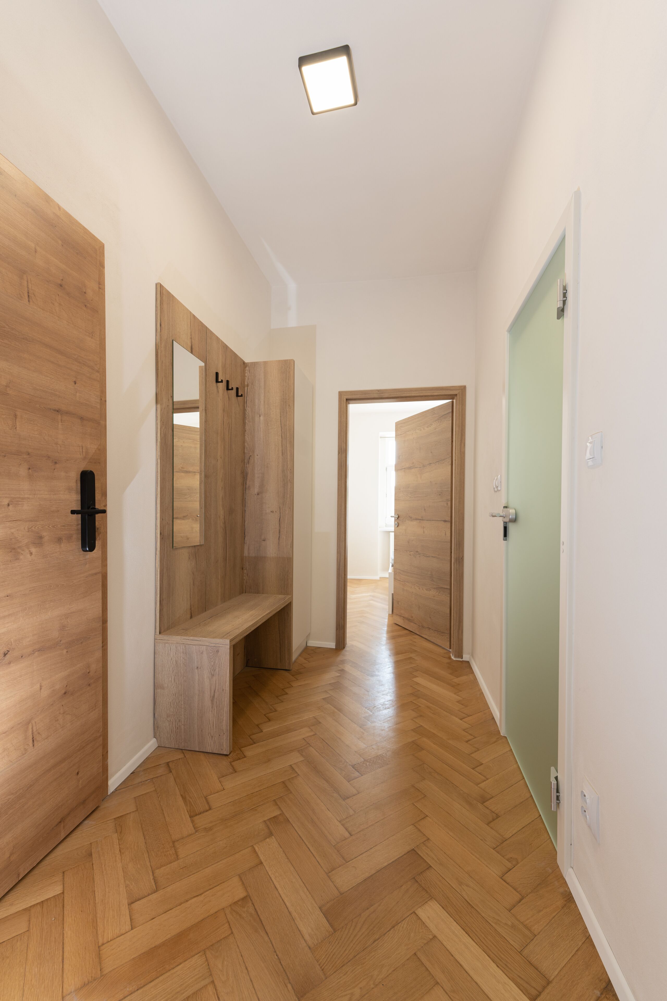 A hallway with wooden walls and a bench, leading to a door with a green frame.
