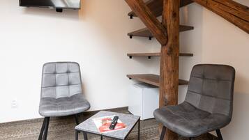 A room with two grey chairs, a small table with a magazine, a TV mounted on the wall, and a wooden staircase.