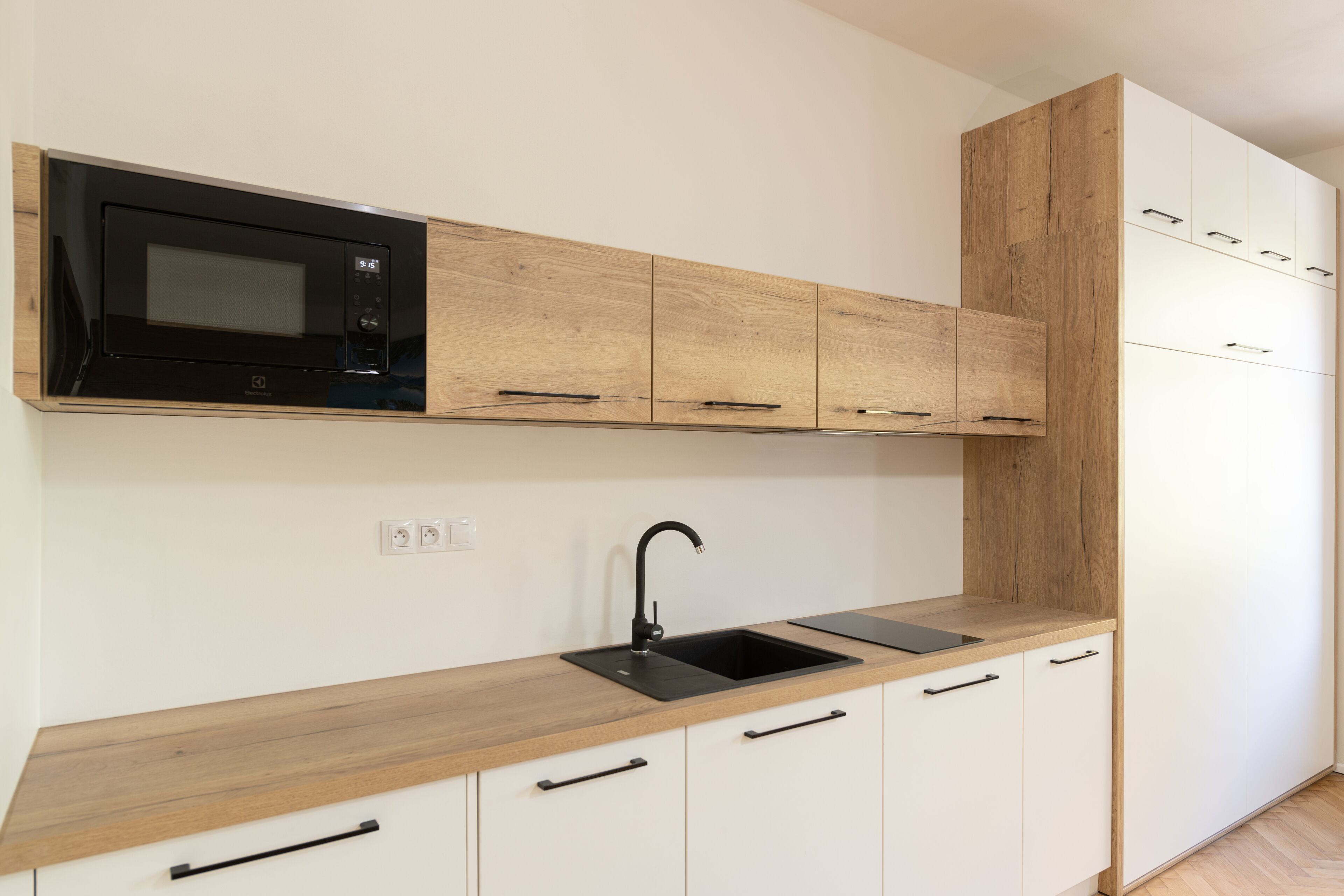 A modern kitchen with a built-in microwave, a sink, and wooden cabinetry.