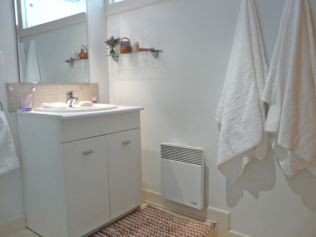 A bathroom with a white sink, mirror, and towel rack. There are shelves above the sink holding toiletries.