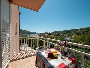 A balcony with a table set for a meal, overlooking a scenic view of a lake and hills. - Apartments Njirić  (Dubrovnik)