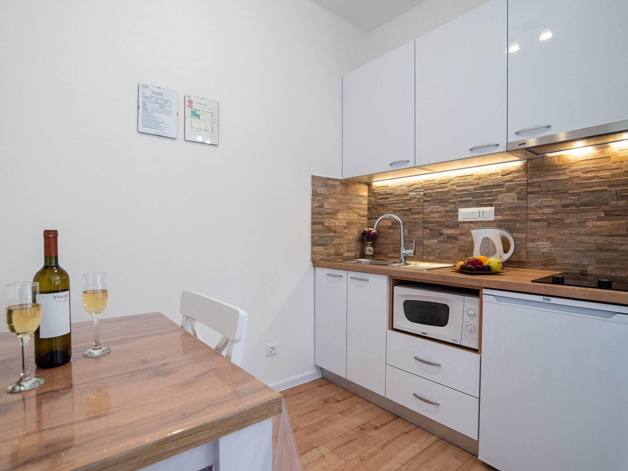 A modern kitchen with white cabinets, a wooden countertop, a built-in oven, and a stone backsplash.