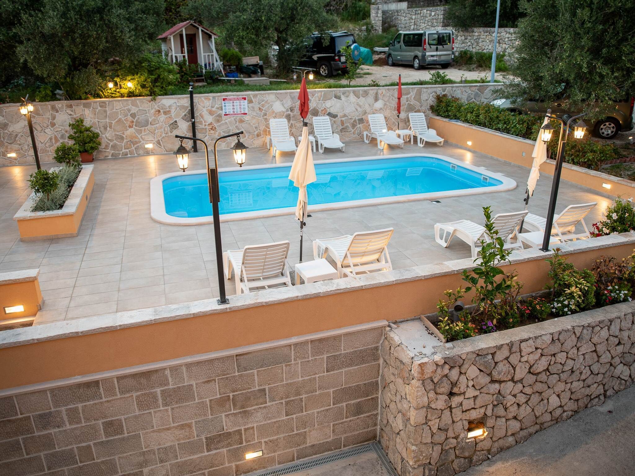 An outdoor swimming pool with lounge chairs and umbrellas, surrounded by stone walls and potted plants.