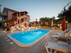 A swimming pool with lounge chairs and a building with a balcony. - Apartments Njirić  (Dubrovnik)