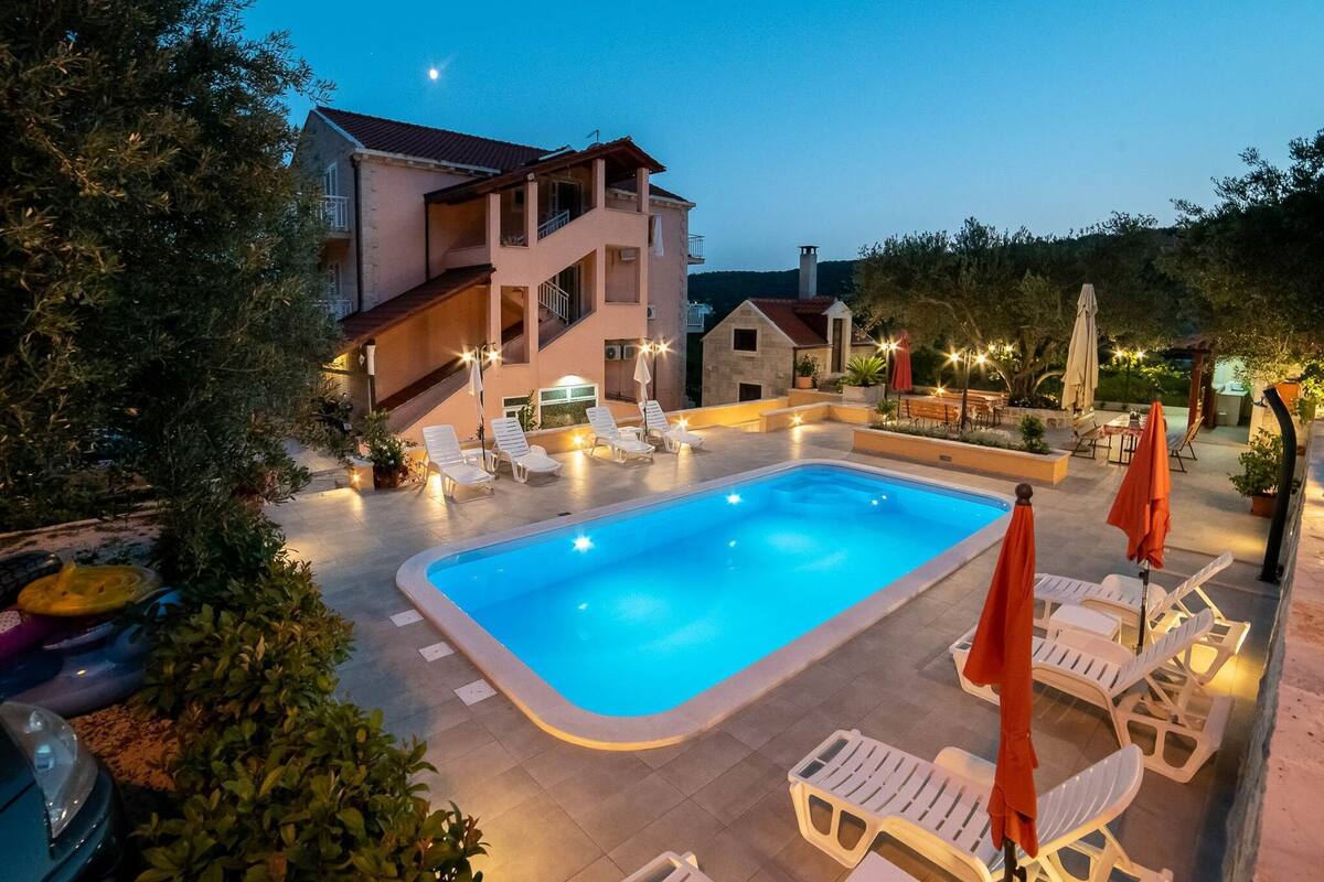 Une piscine entourée de chaises longues et de parasols, le tout bordé par un bâtiment doté d’un balcon et d’un escalier.