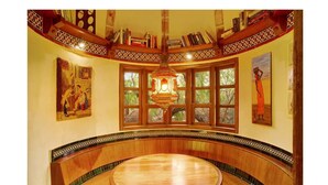 Une pièce dotée d’un banc en bois aux lignes courbes, d’une grande fenêtre à carreaux et d’un plafond décoratif orné de motifs complexes.