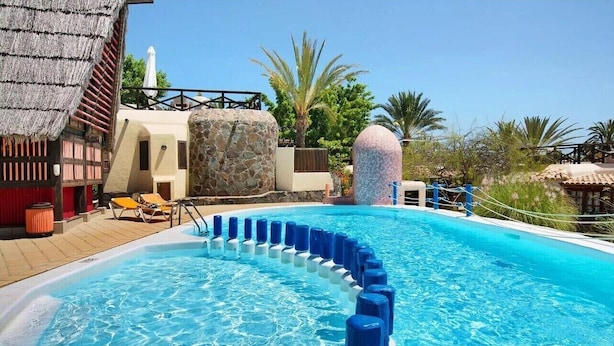 Une piscine à l’eau bleue, entourée de chaises longues et d’un mur de pierre.