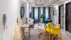 A modern living room with a glass dining table, yellow chairs, a blue sofa, and a white coffee table. - George Residence (Lekki)
