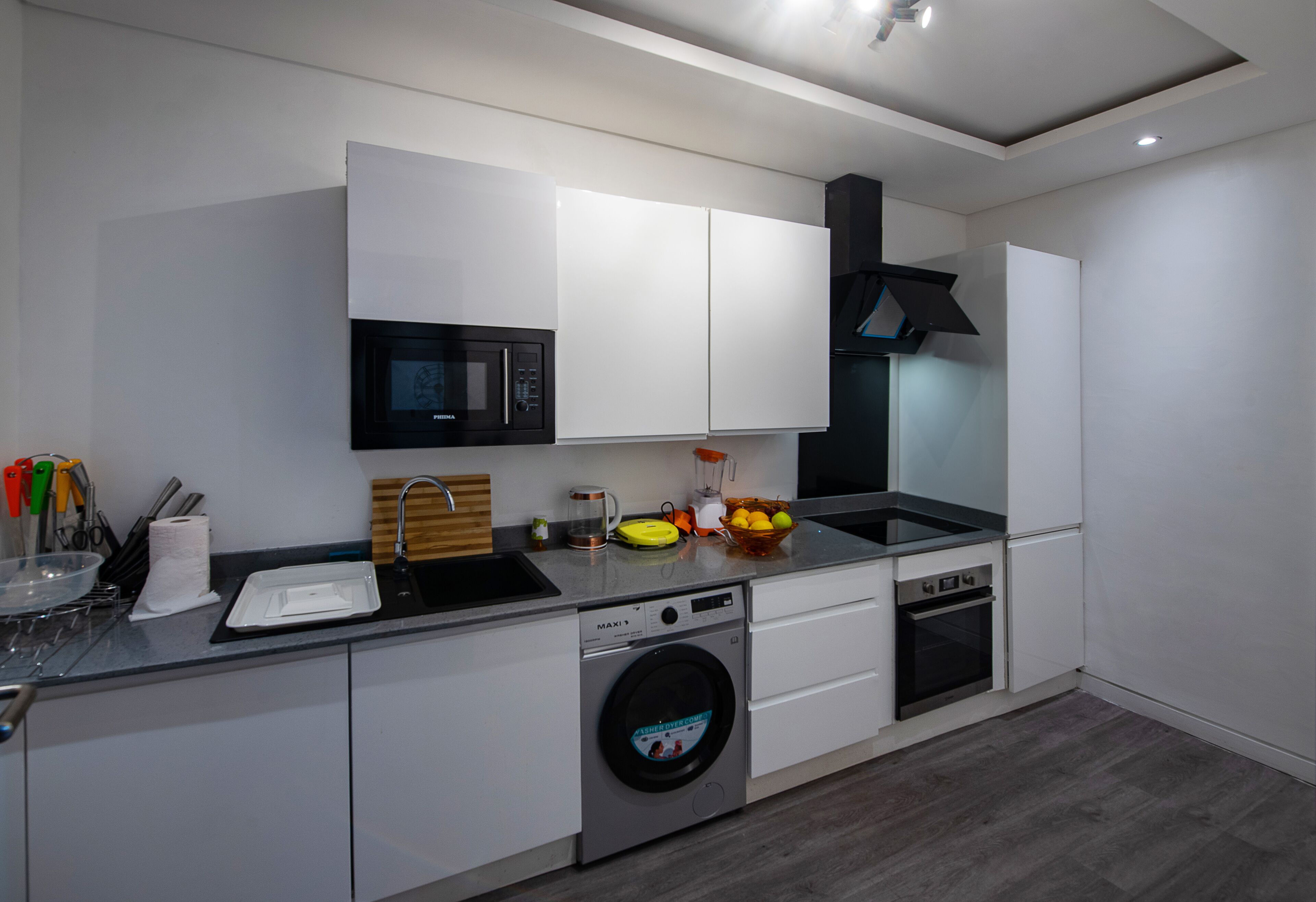 A modern kitchen with white cabinets, a built-in microwave, a dishwasher, and a washing machine.