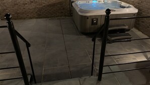 Un bain à remous doté d’un panneau de commande et de marches menant à celui-ci, entouré de carreaux de pierre et d’un mur en briques.