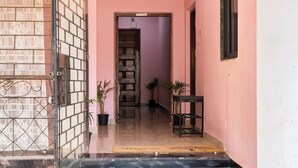 A set of marble stairs leading to a door with a metal gate, a small table, and potted plants in a hallway with pink walls. - Rustic Pvt 2bhk Villa w/ Fiber Net - Dar AlSalaam (Pilar)