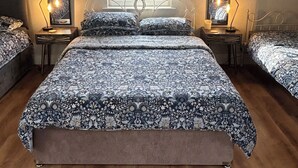 A bedroom with a large bed, two bedside tables with lamps, a window with a view of greenery, and two wall mirrors.