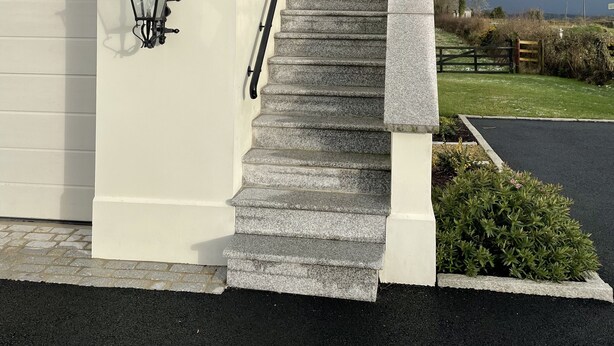 A building with a white exterior, a set of stone steps leading to a garage, and two black wall-mounted lanterns.
