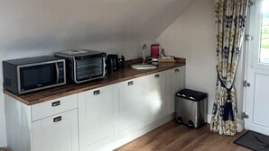 A compact kitchen with white cabinets, a wooden countertop, a microwave, a toaster, and a trash bin.