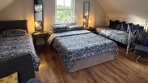 A bedroom with a sloped ceiling, two beds with matching bedding, a nightstand, a dresser, and a window with a view of greenery.