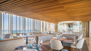 A modern dining area with round tables, cushioned seating, and large windows offering views.