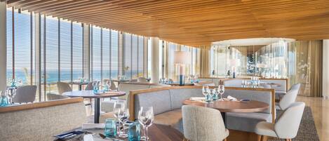 Un espace repas moderne avec des tables rondes, des sièges confortables et de grandes fenêtres offrant une vue panoramique.
