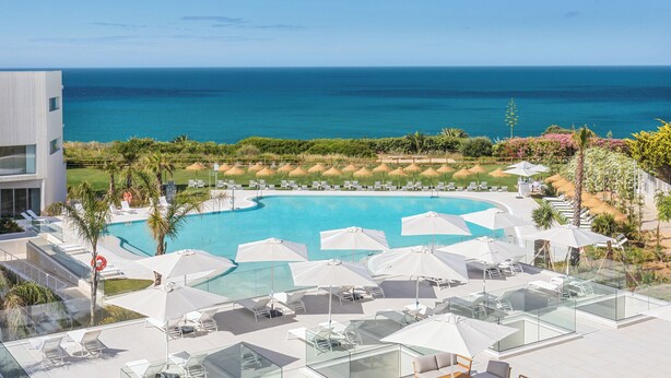 A modern hotel with a pool, outdoor seating, and a view of the ocean.