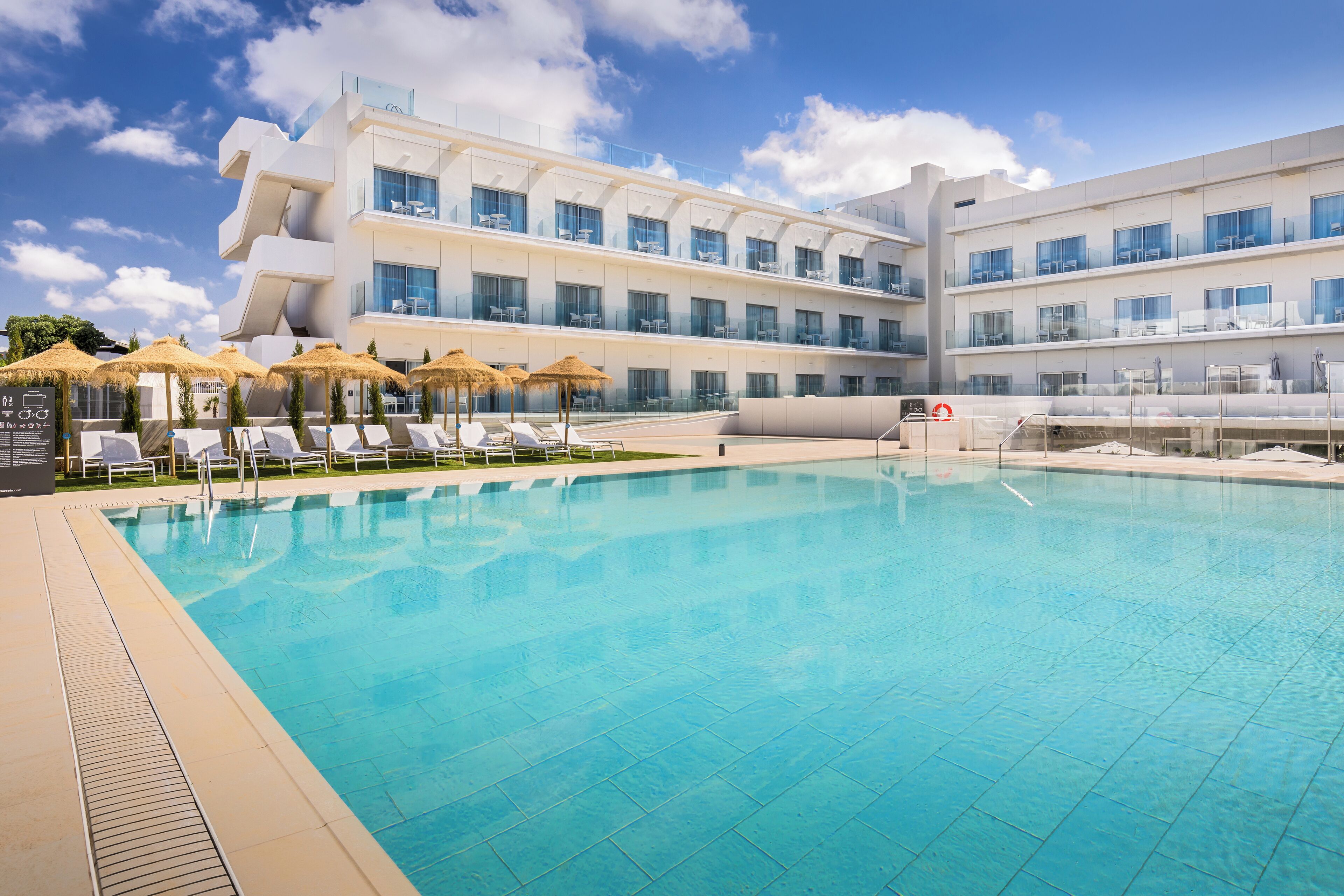 Un hôtel moderne doté d’une grande piscine, de chaises longues et de parasols.