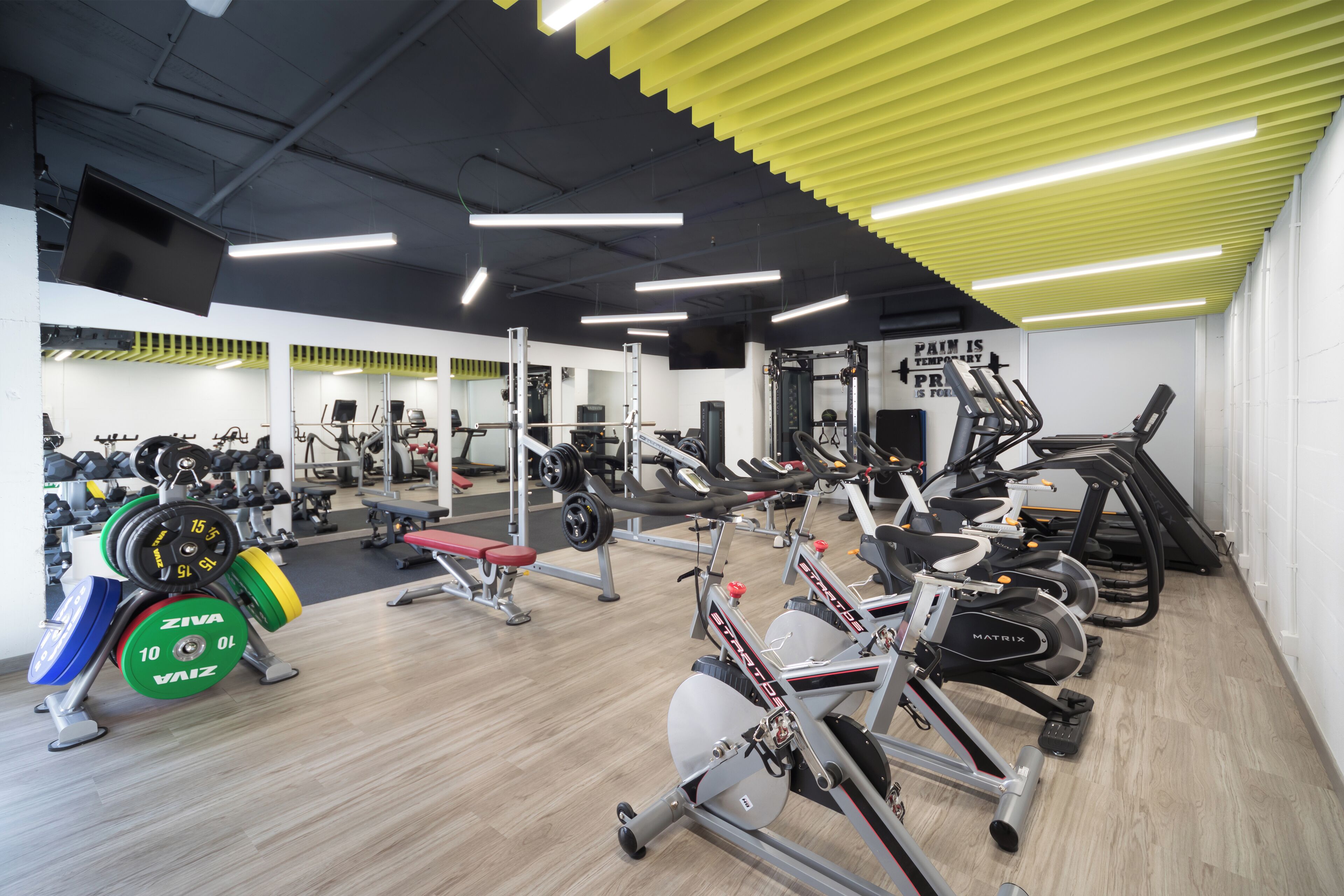 A gym with various exercise equipment, a weight bench, and a mirror wall.