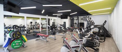 A gym with various exercise equipment, a weight bench, and a mirror wall.