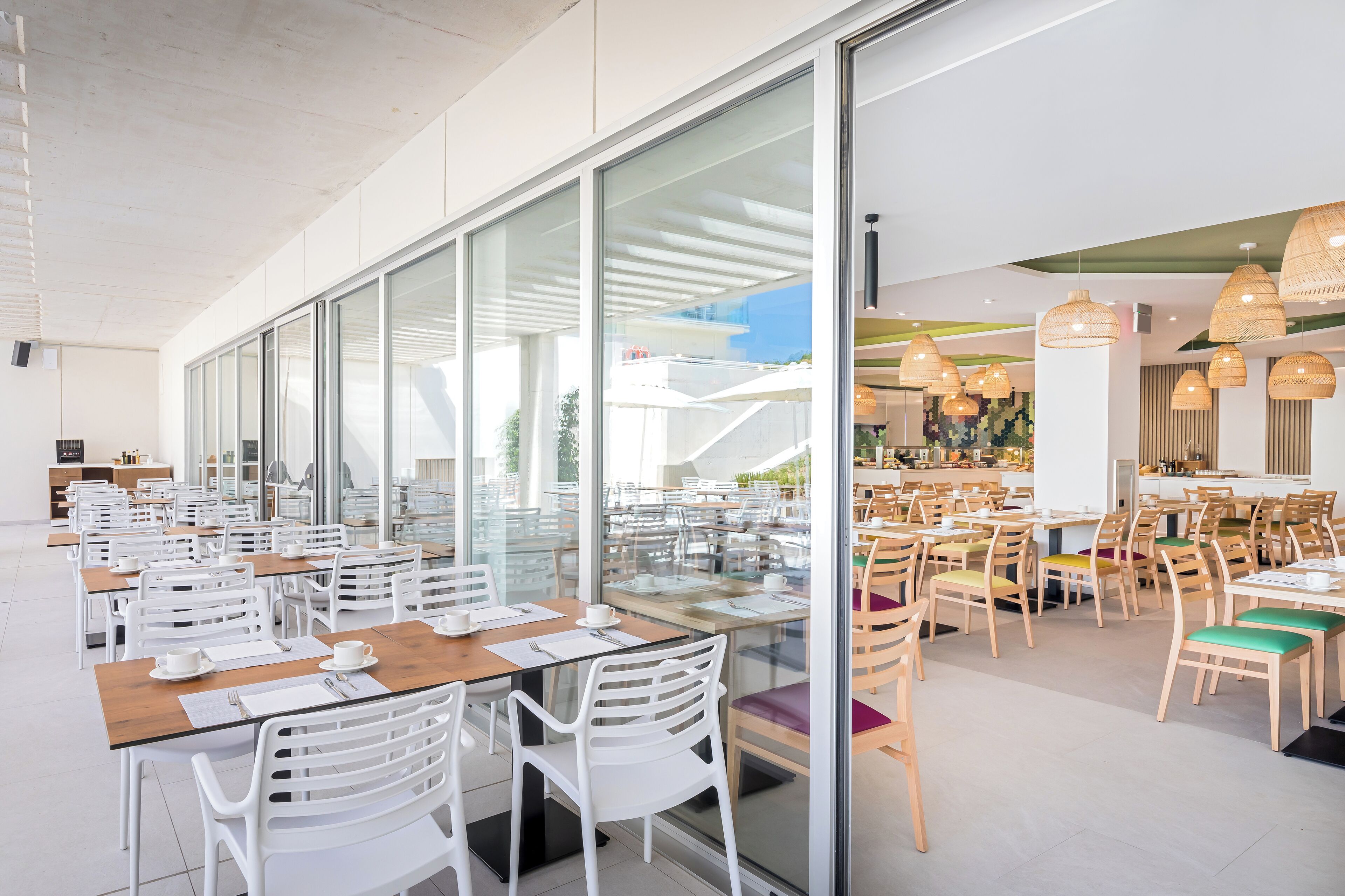 A spacious indoor dining area with multiple tables and chairs, large windows, and hanging light fixtures.