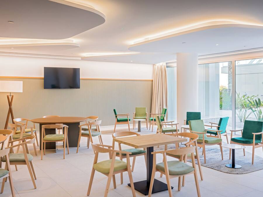 Habitació d'hotel moderna amb una taula rodona gran, diverses cadires, un televisor de pantalla plana fixat a la paret i grans finestres que donen a l'exterior.