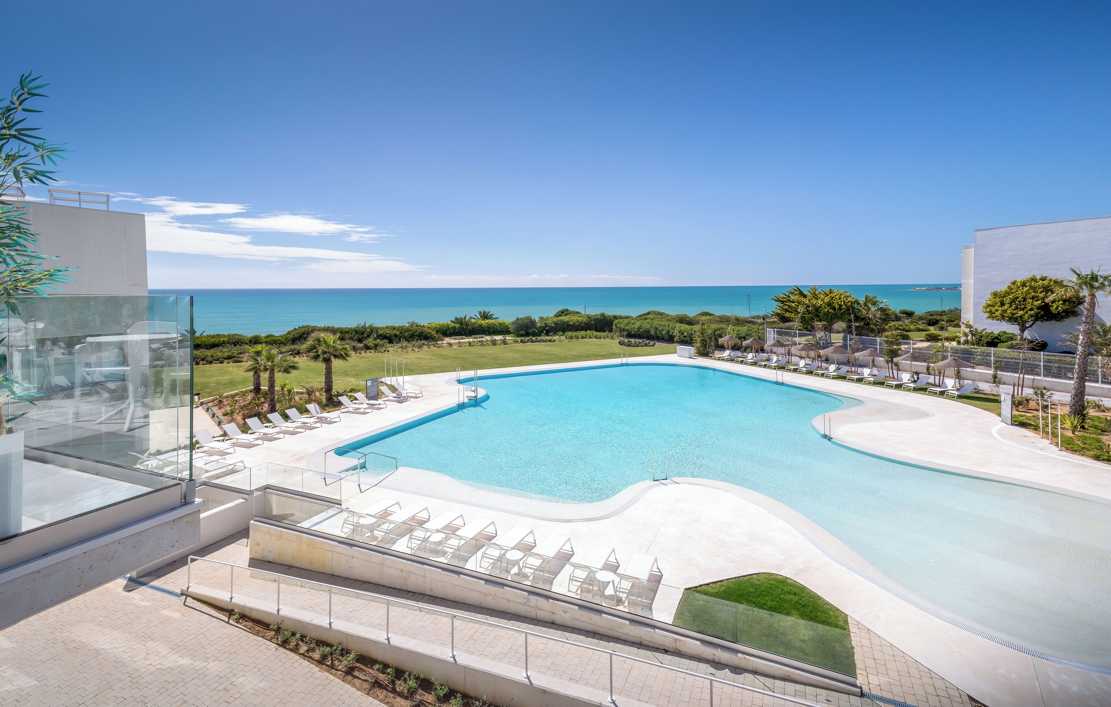 A modern pool area with clear blue water, surrounded by lounge chairs and a view of the ocean.