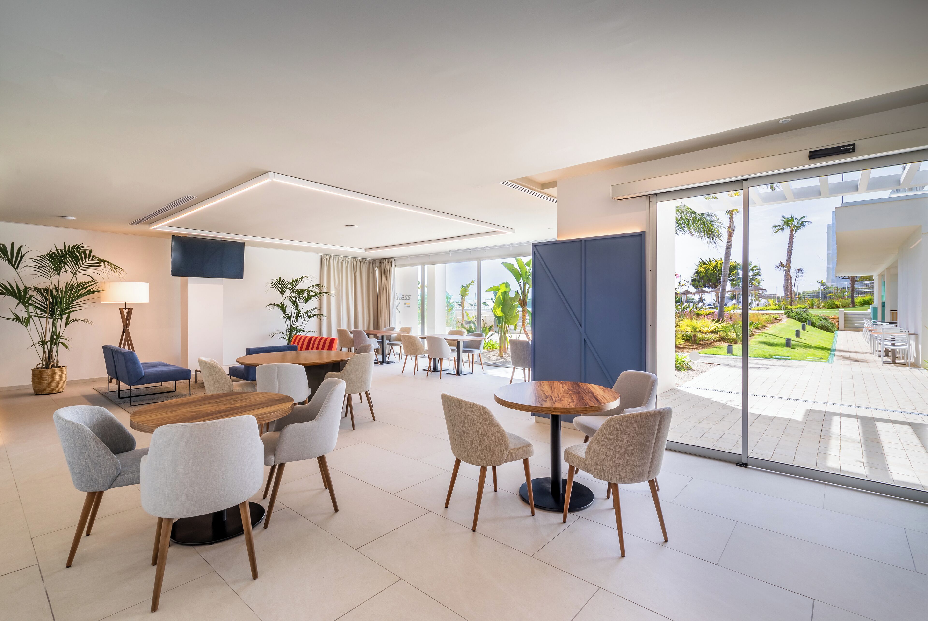 Un moderno vestíbulo de hotel con una mesa y sillas de madera, un sofá y un ventanal con vistas al jardín exterior.