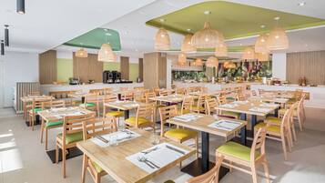 A spacious dining area with multiple tables and chairs, a central bar, and pendant lighting.