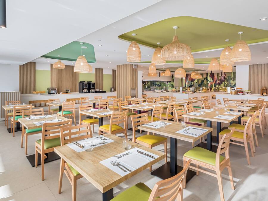 A spacious dining area with multiple tables and chairs, a central bar, and pendant lighting.