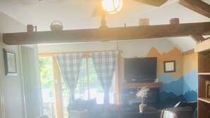 Zona pranzo con tovaglia a quadri, sedie di legno, ventilatore a soffitto e televisione sullo sfondo.