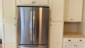 Un frigorifero in acciaio inox in cucina, con mobili bianchi e un piano di lavoro in legno.