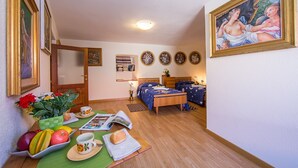 A cozy room with a wooden floor, a bed with a blue bedspread, a small table with fruits and a book, and a painting on the wall. - Terrazza Vista Menaggio (Plesio)