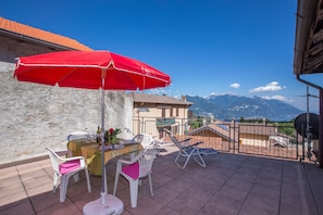 Una terraza con una sombrilla roja, sillas blancas y una mesa con botellas y vasos.