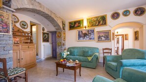 A cozy living room with a stone fireplace, a green sofa, and a wooden cabinet with decorative items. - Terrazza Vista Menaggio (Plesio)