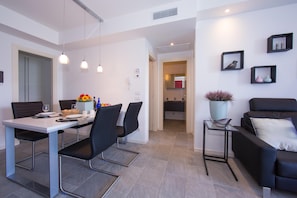A modern living room with a sofa, a dining area with a table and chairs, and a kitchen in the background.