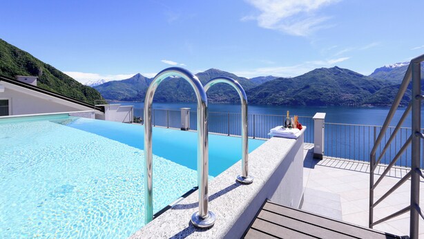 A rooftop pool with clear blue water, metal pool ladders, and a view of mountains and a lake. - Casa Laura Apt. 3 (Plesio)