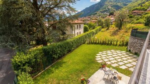 A courtyard with a stone patio, a small table with chairs, and a view of a hillside village. - Lenno Dolcelago (Tremezzina)