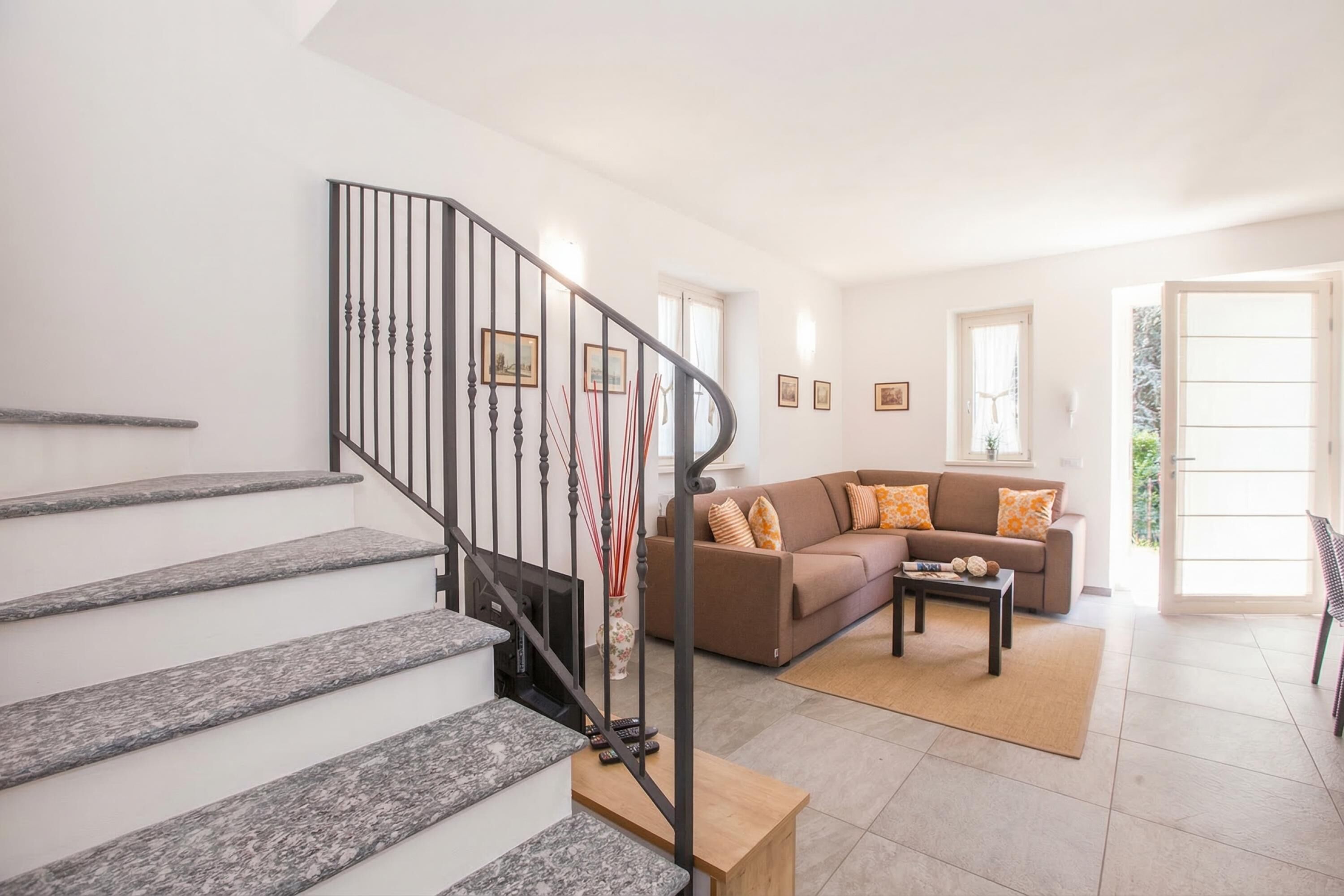 A staircase with a black railing, a brown sofa with orange and white cushions, and a wooden coffee table.