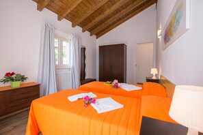 Un dormitorio con dos camas, vigas de madera en el techo, una ventana con cortinas, un aparador, un armario y un cuadro en la pared.