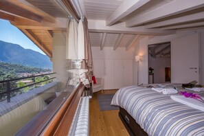 Ein Schlafzimmer mit einem großen Bett, einem Fenster mit Vorhängen, Blick auf Berge und einem Balkon.