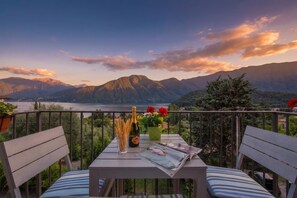 Ein Balkon mit Tisch, Stühlen, einer Flasche, Gläsern und Blumen.