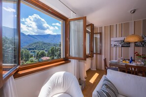 Quarto com uma grande janela, área de jantar e vista para montanhas.